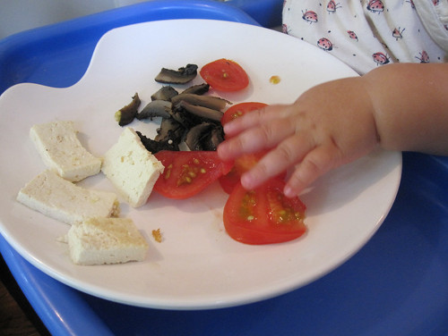 13-month old child picking up tomatoes, tofu, and mushrooms off their plate.